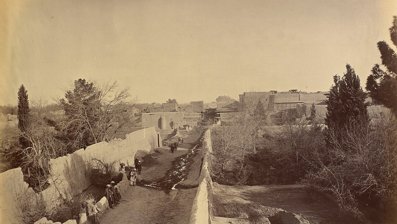 A black-and-white photograph of a long road between high stone walls running through Jalalabad.