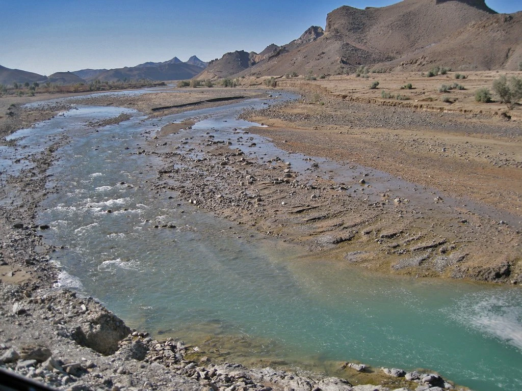 A shallow river running over a wide gravel bed between low hills