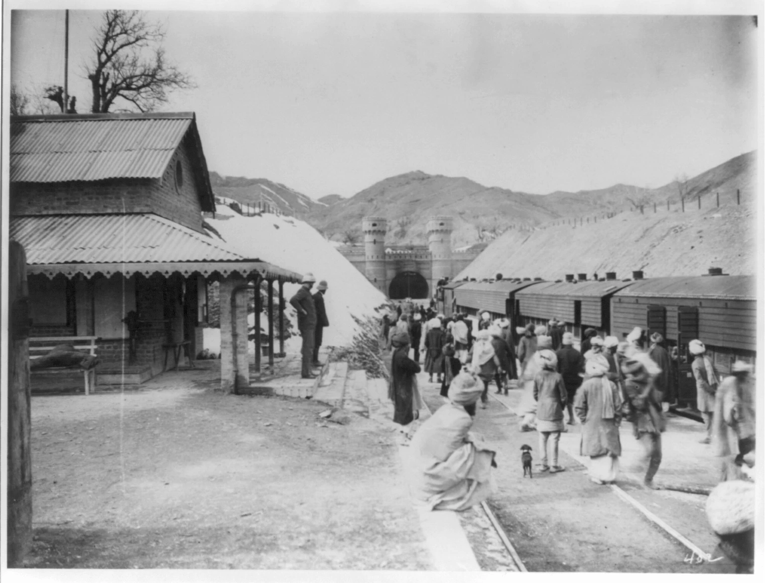 Black-and-white photograph of a small railway station below bare hills