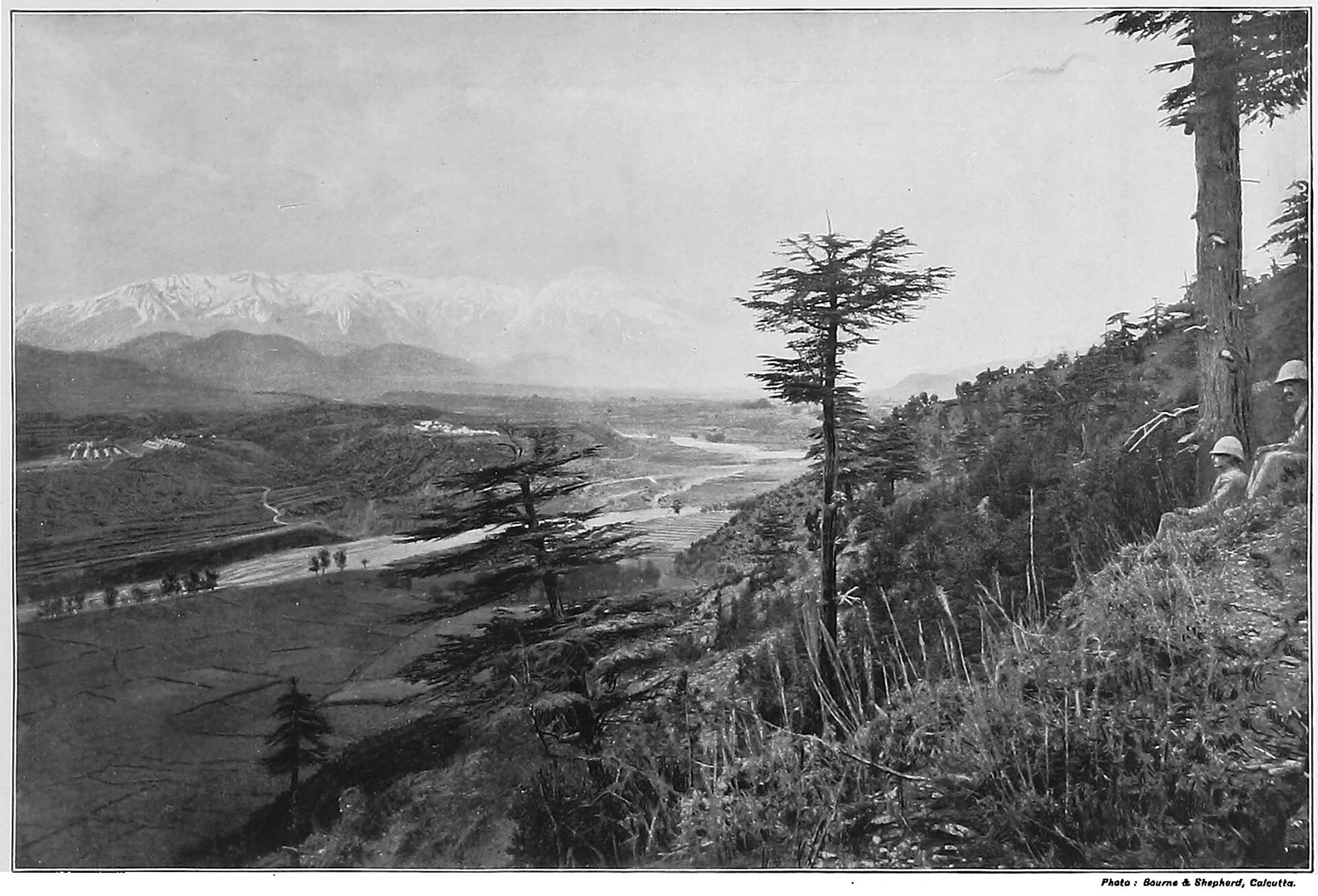 A broad valley with rows of army tents below mountains