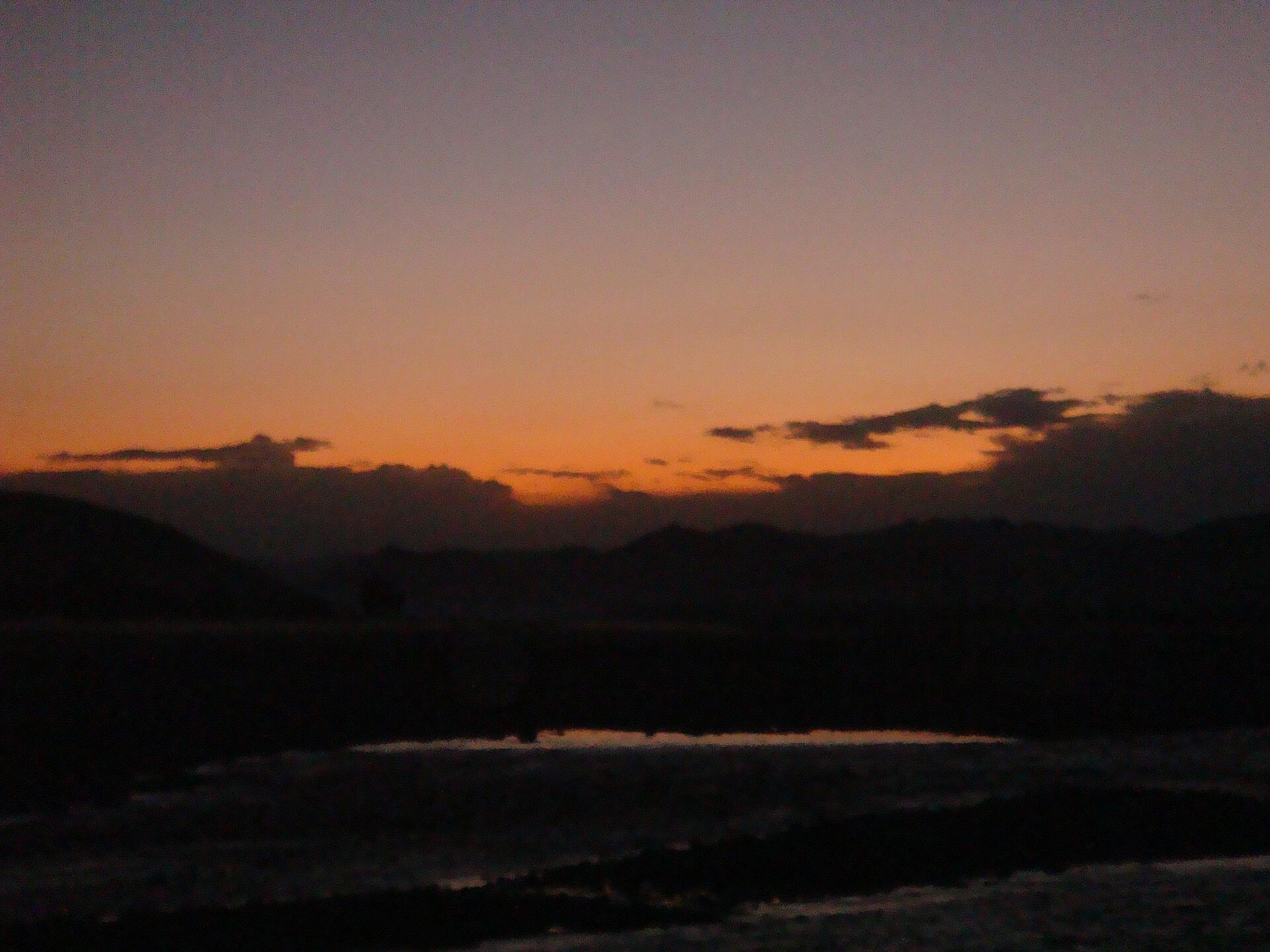 Dark hills against an orange evening sky above a wide, shallow river bed
