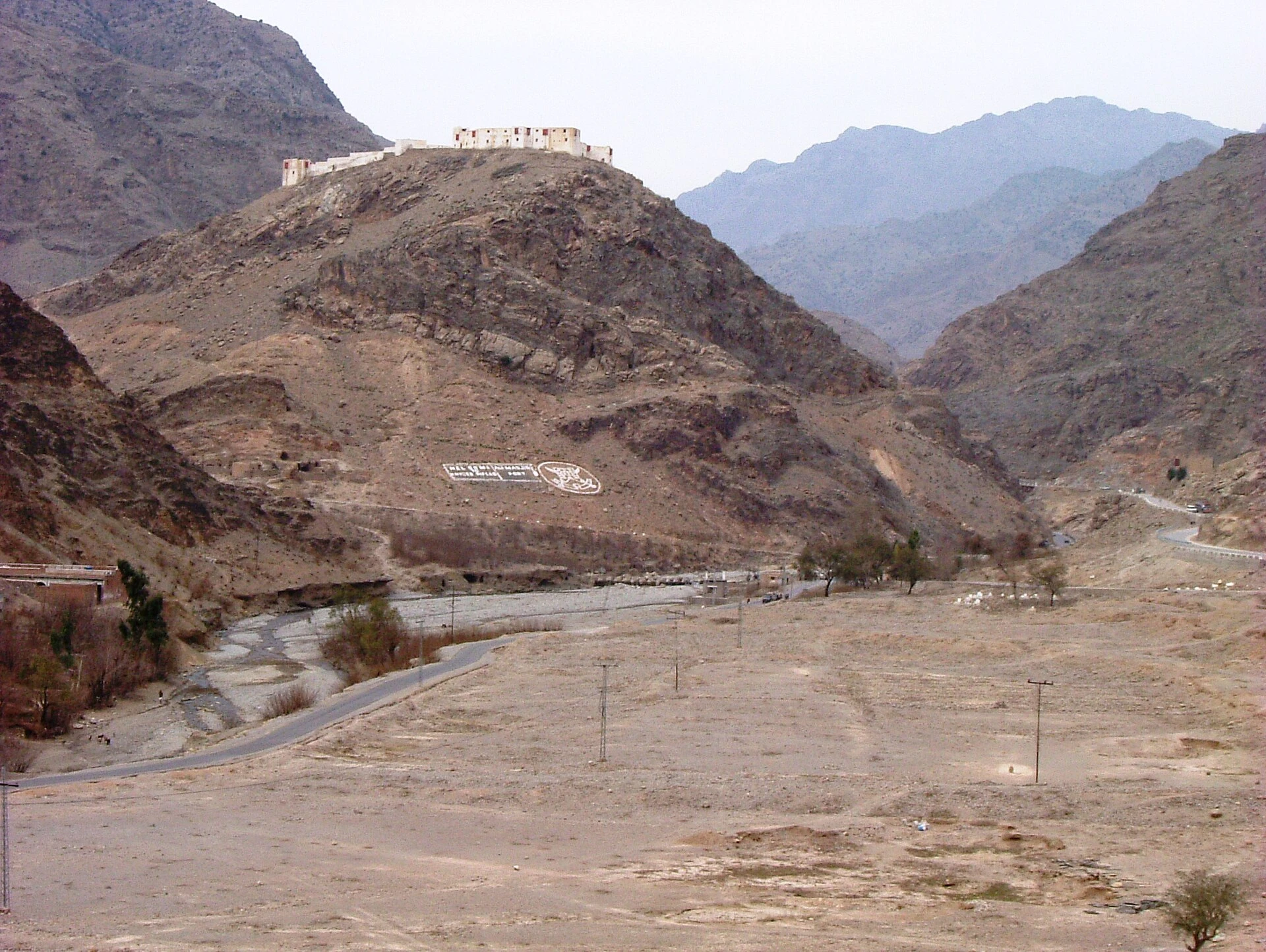 A stone fort on a rocky ridge above a narrow valley with a road
