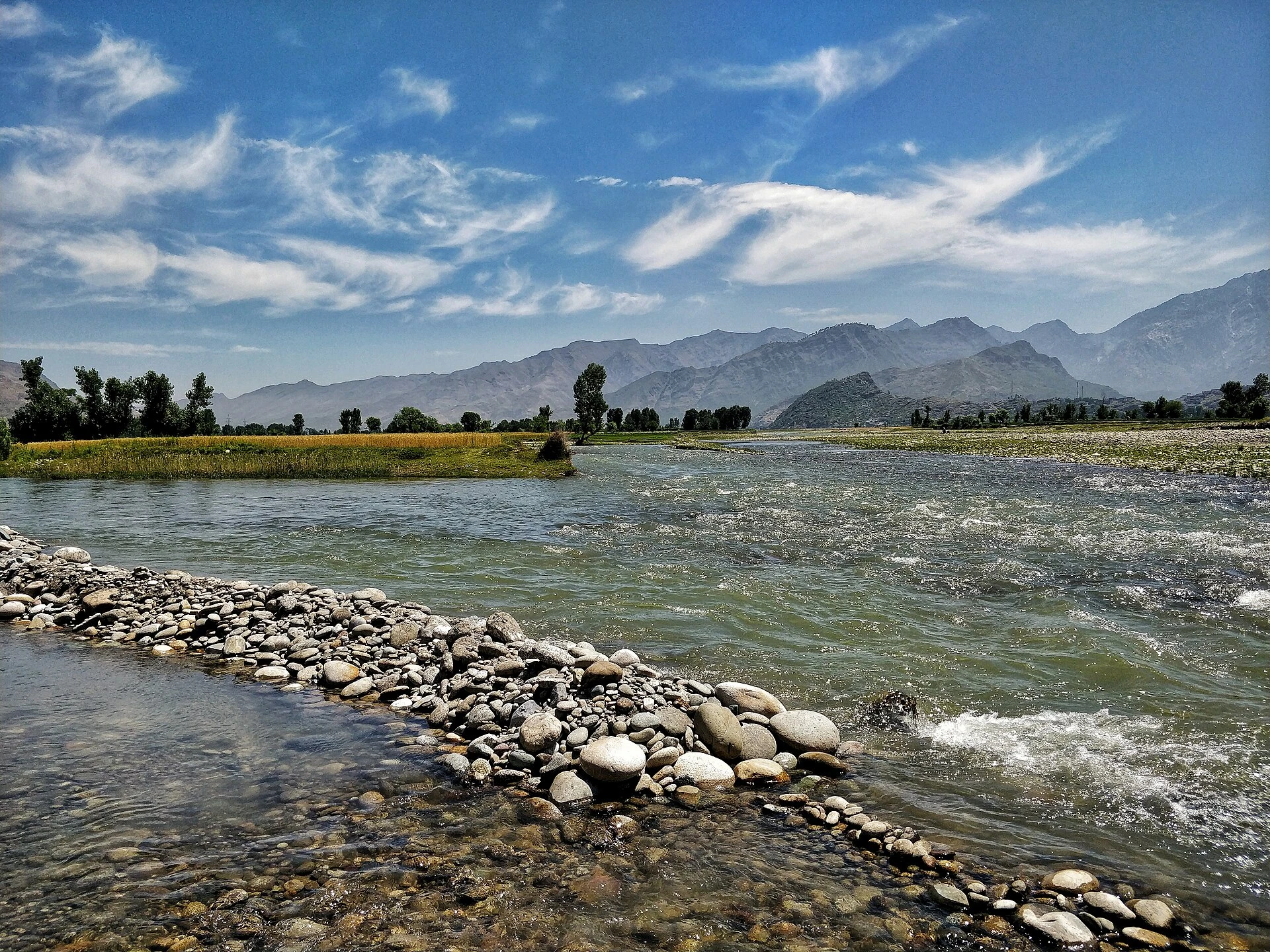 A wide, shallow river flowing between low hills