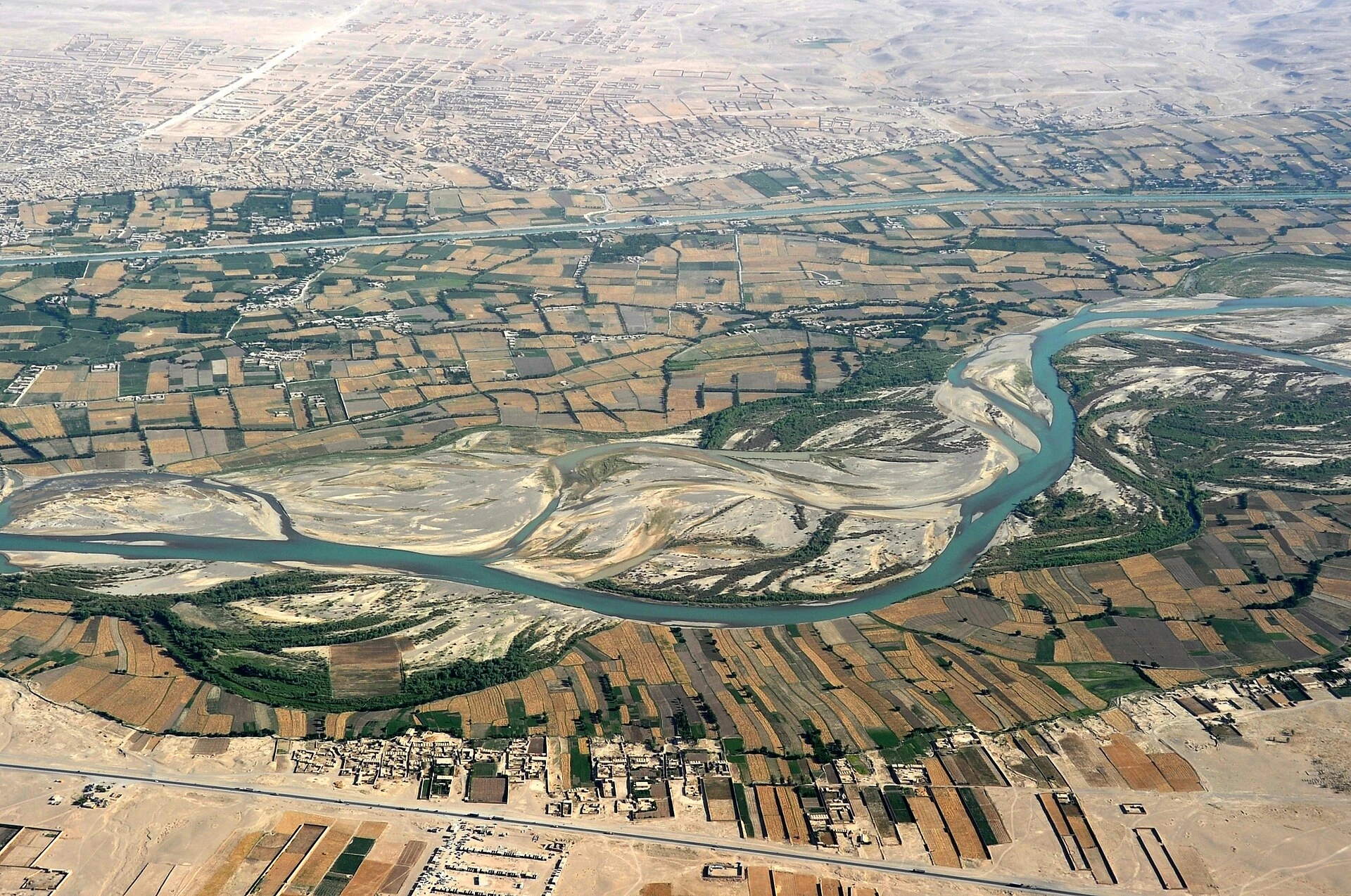 Aerial view of a wide river with green fields and a canal, and a town in the distance