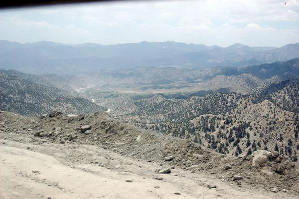 A dirt road at the top of a pass looking down over pine-dotted ridges