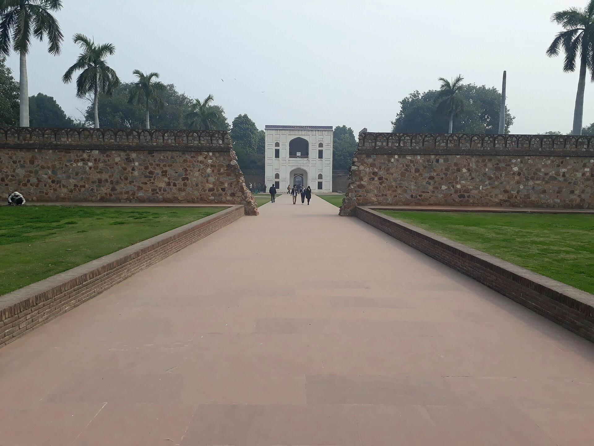 A stone path between lawns leading to an arched gateway in a battlemented wall