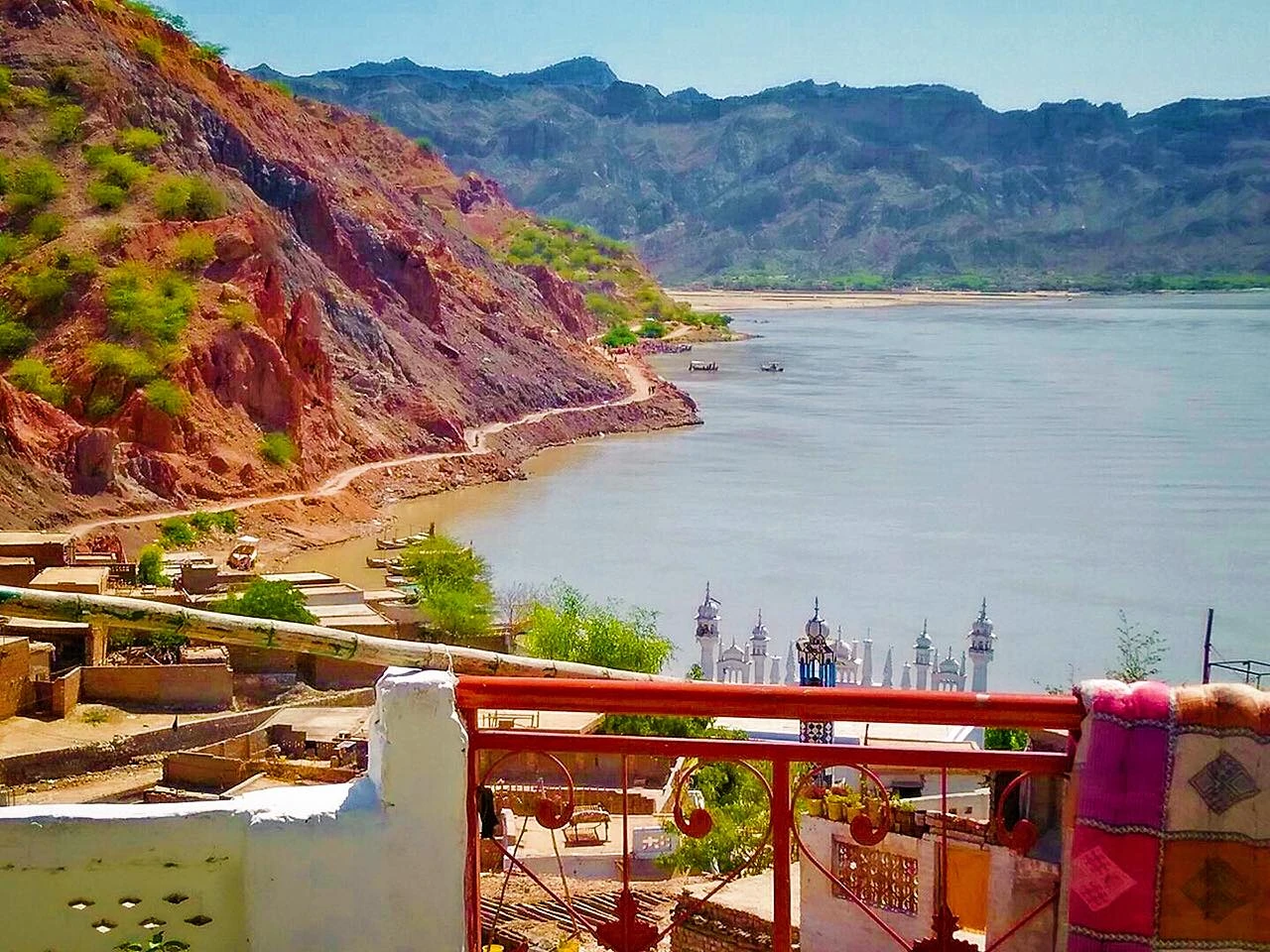 The broad Indus river below red hills, seen over the rooftops of a town